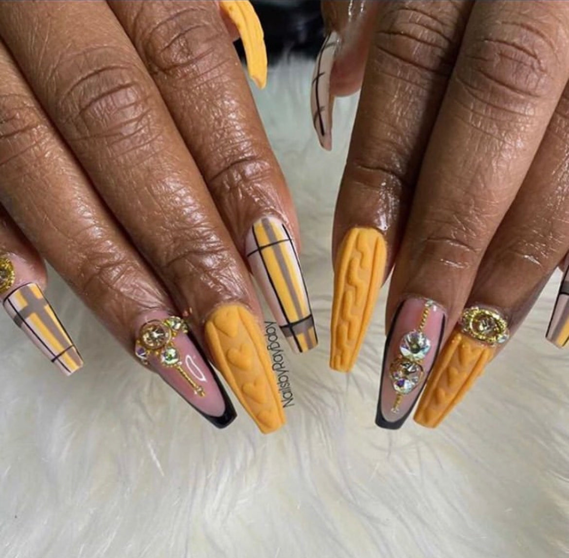 Long coffin nails with a mustard yellow textured cable-knit sweater design, plaid accents and gold charms, on white faux fur.