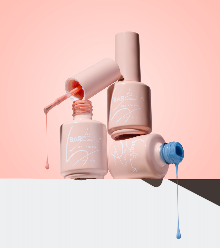 Stacked peach BarBella Co. polish bottles on a pink background, with coral and blue polish dripping from open bottles.