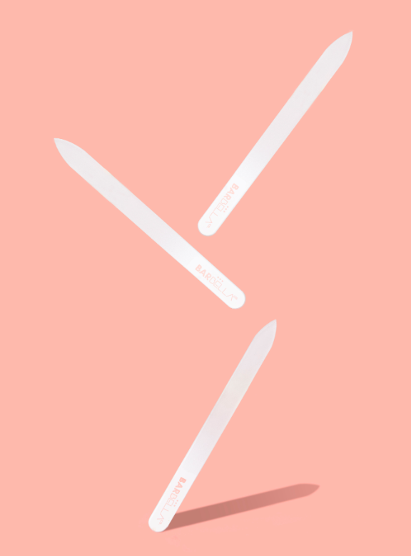 Three white glass nail files on a peach background.