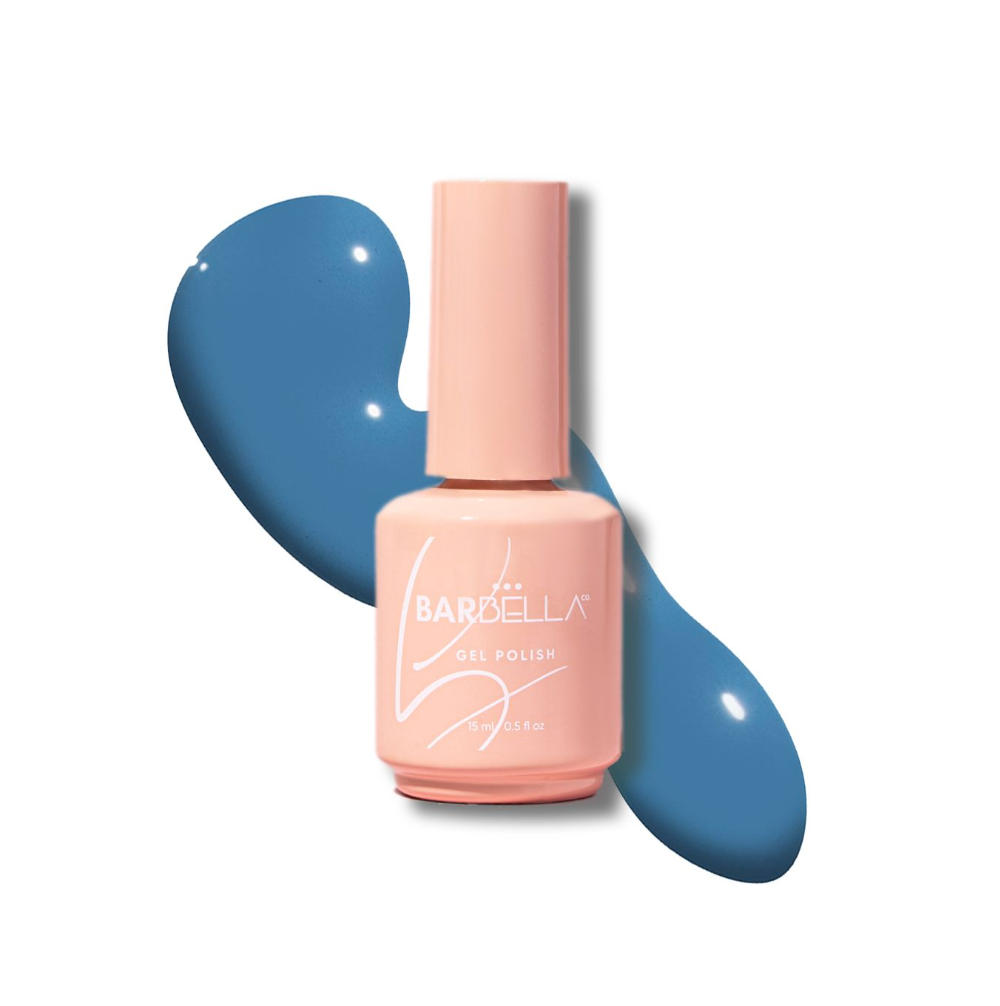 Peach BarBella Co. polish bottle on a swatch of muted denim blue polish, the blueberry milk nail color.