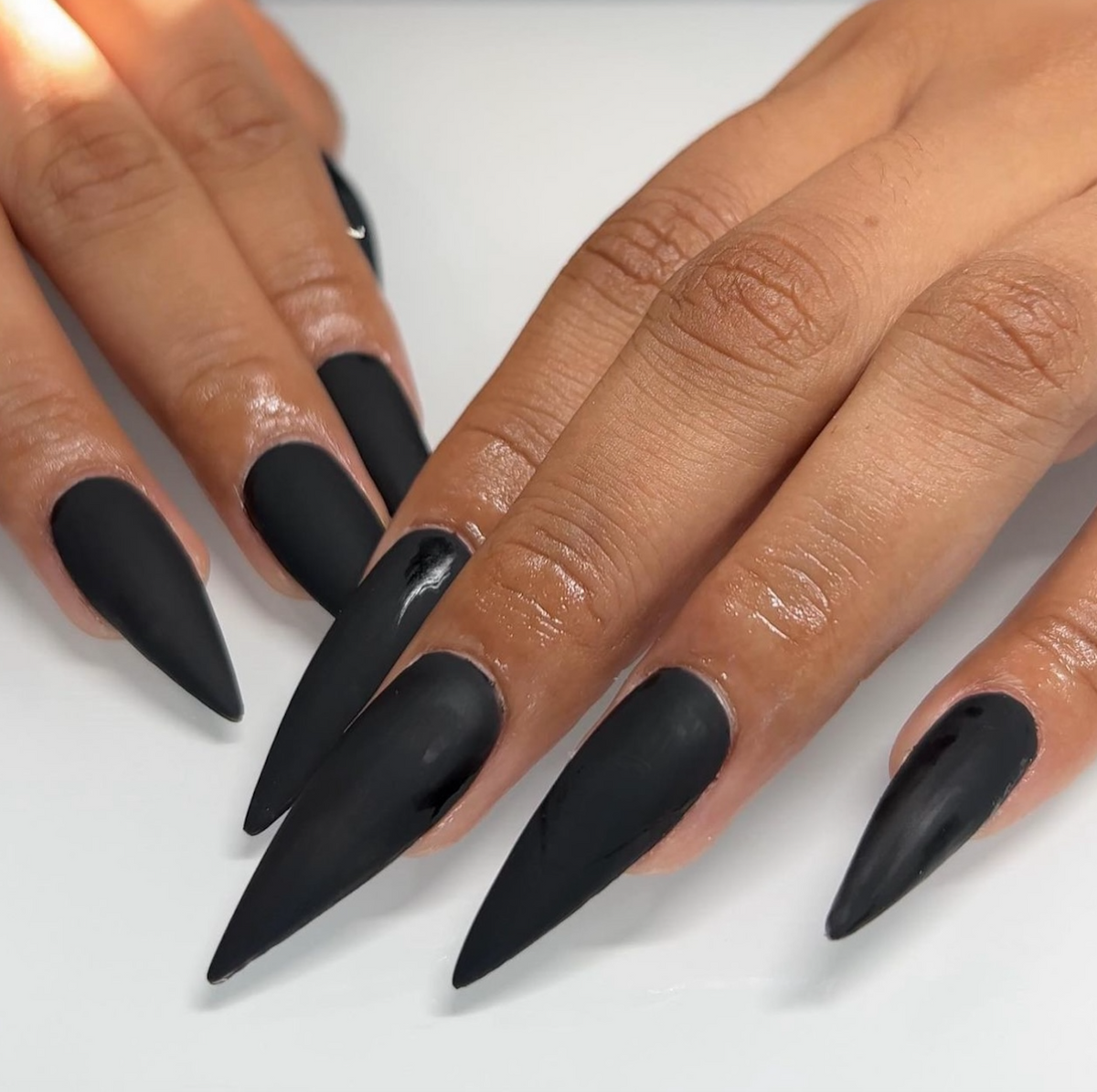Long matte black stiletto nails on a white background.