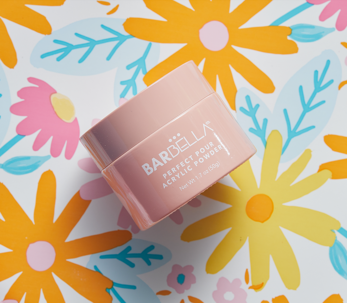 Peach BarBella Co. jar on a bright floral print with orange, yellow, pink and teal flowers.