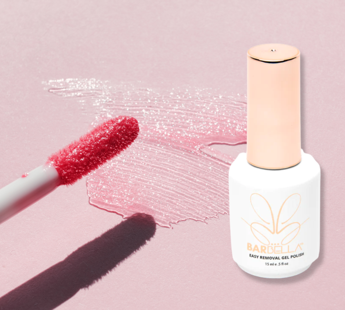 Pink lip gloss wand and a shimmery gloss smear beside a white and gold BarBella Co. bottle on a pink background. Inspiration for glossy lip gloss nails.